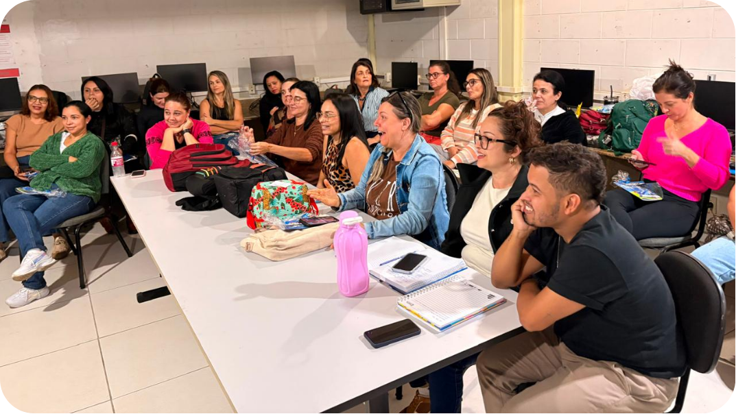 Professores sentados em volta de uma mesa conversam e sorriem durante a formação